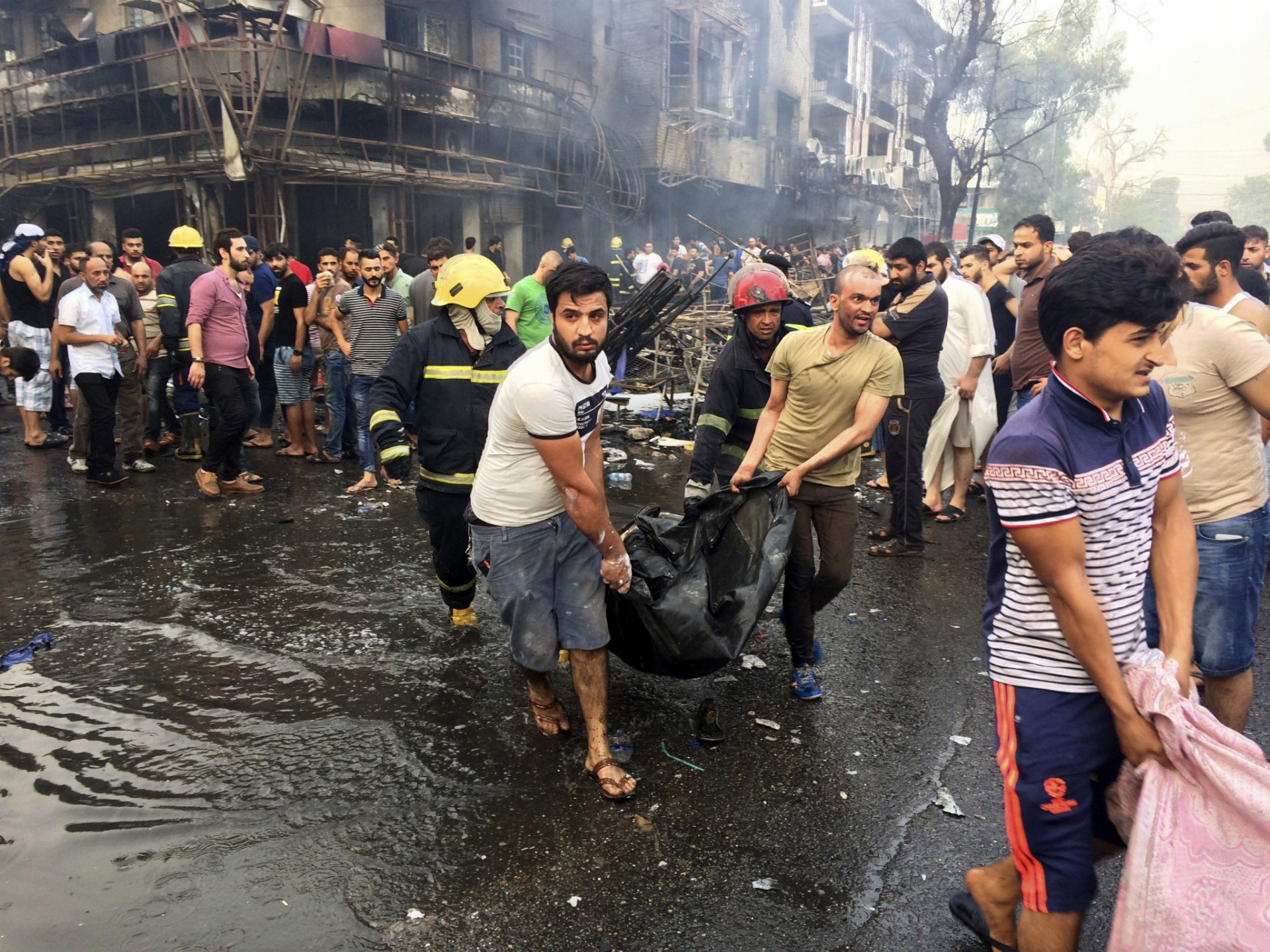Hasiči a civilisti odnášajú telá obetí bombového útoku v rušnej štvrti Karráda v irackom hlavnom meste Bagdad 3. júla 2016. Prvá nálož nastražená v dodávke explodovala neďaleko reštaurácie a nákupného strediska v rušnej štvrti Karráda, ďalšia bomba vybuchla krátko nato na prevažne šiitskom predmestí severne od metropoly.
