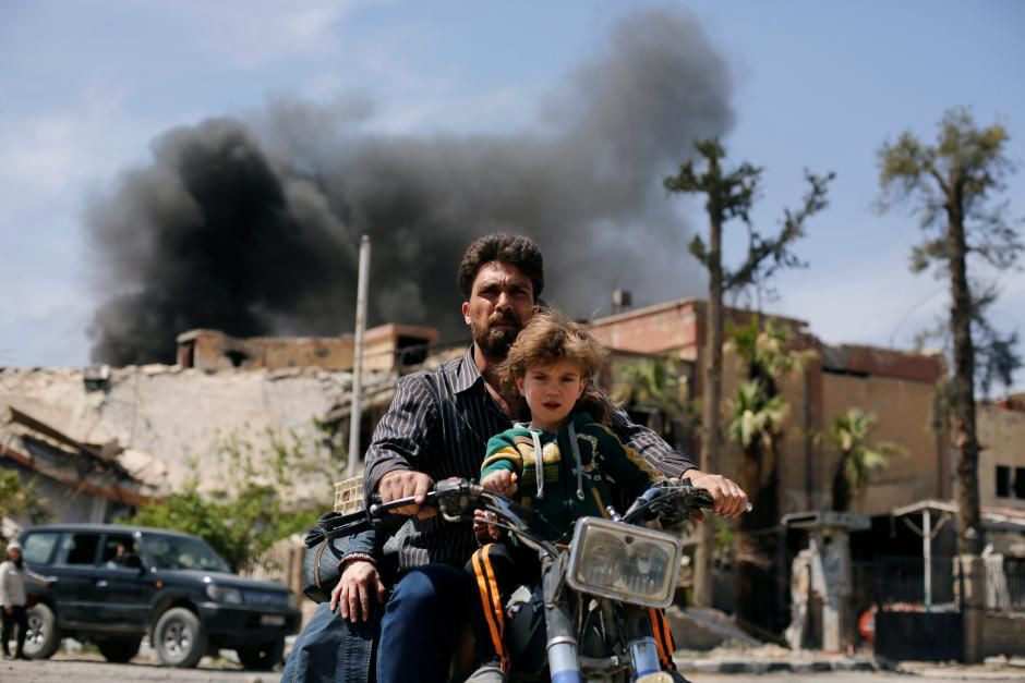 Muž so synom sa vezú na motorke na predmestí Dúmá v Damašku pár dní po údajných chemických útokoch v oblasti.