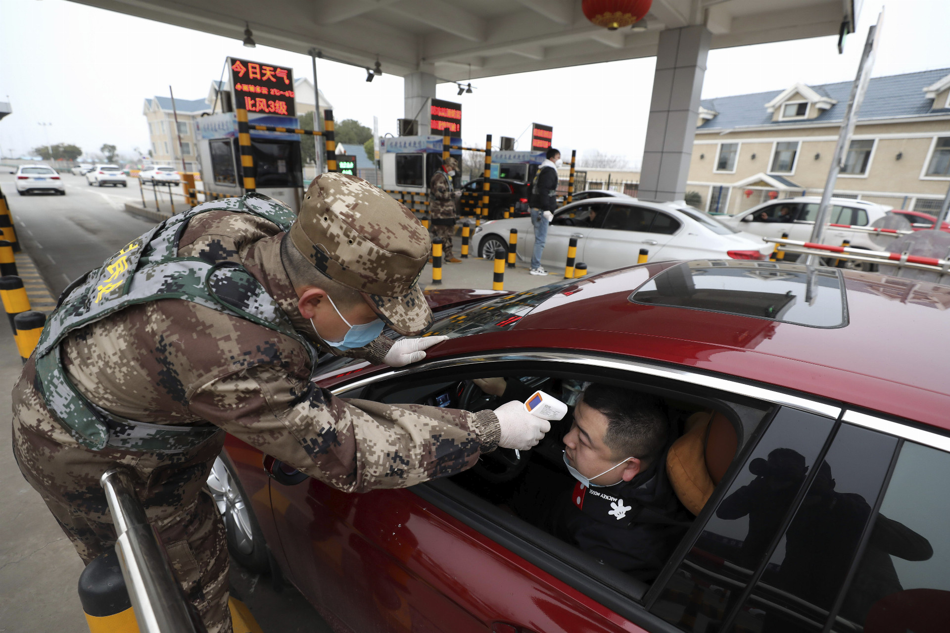 Vojak kontroluje vodičovi teplotu digitálnym teplomerom na kontrolnom stanovišti v čínskom meste Wu-chan.
