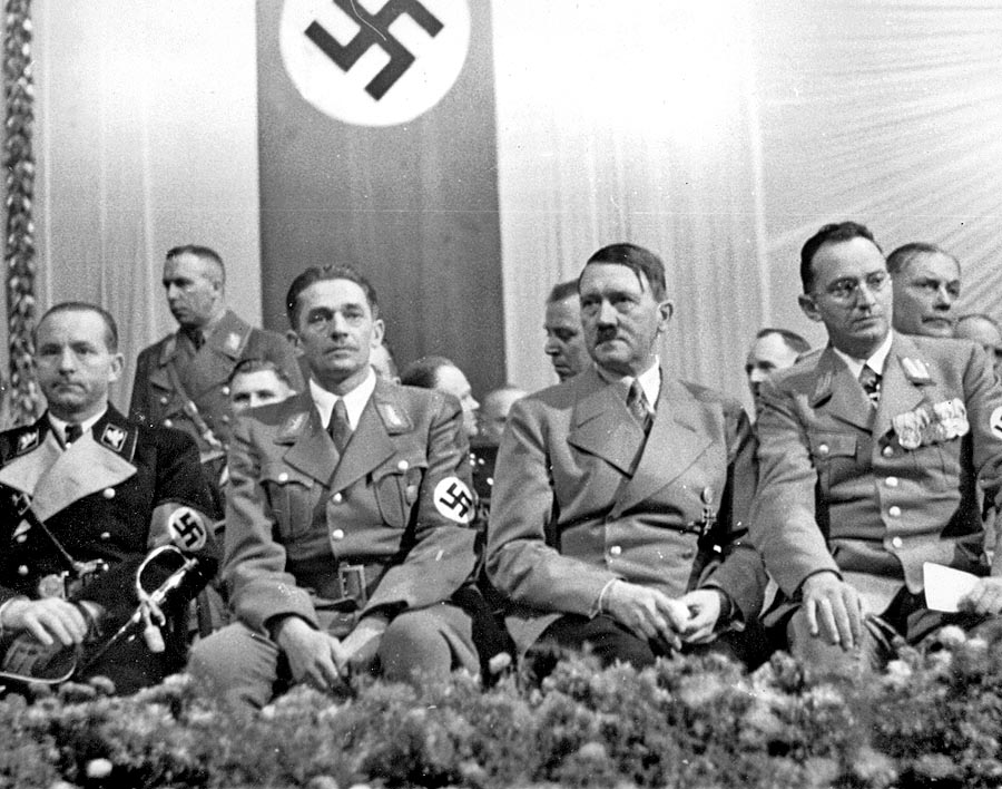 Priamo pod hákovým krížom sedí Karl Hermann Frank, vedľa neho Adolf Hitler a napravo od nacistického diktátora Konrad Henlein. Fotka je z roku 1938 z Liberca.