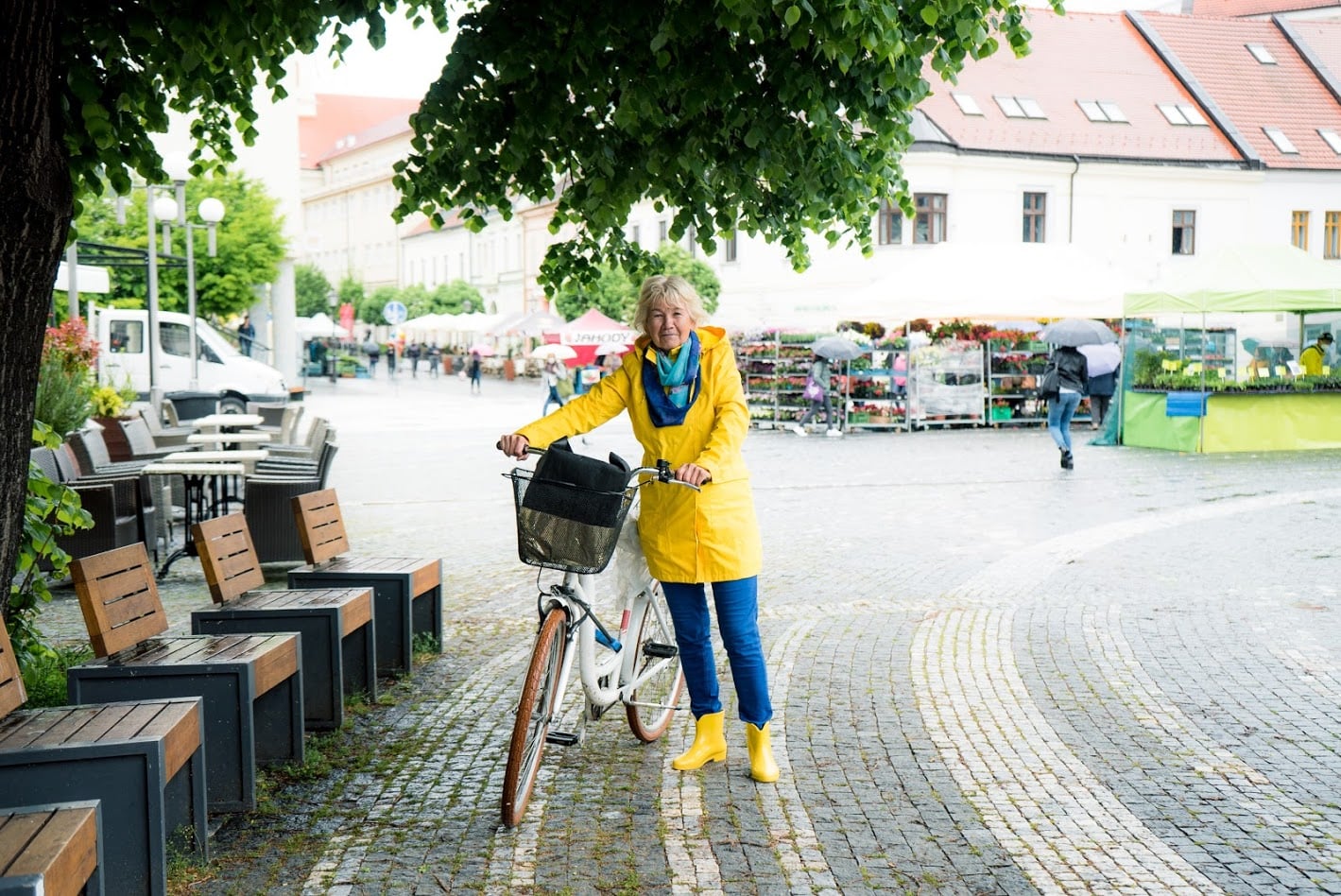 Babka stojí s bicyklom na námestí
