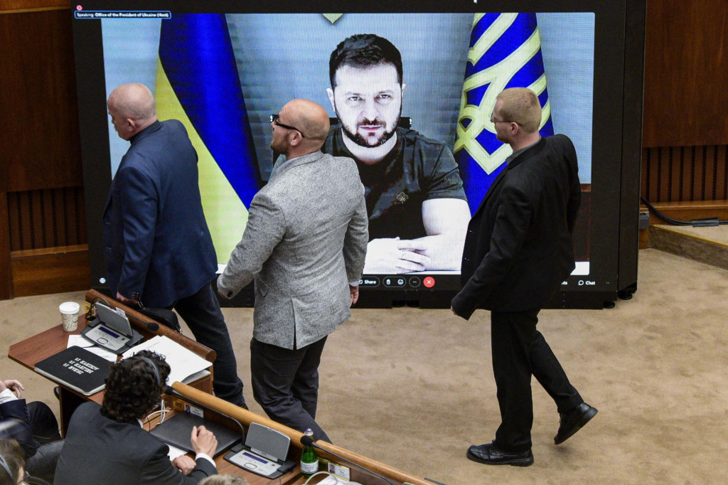 Poslanci pred obrazovskou s ukrajinským prezidentom Volodymyrom Zelenským.