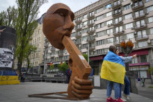 Źeny zahalené do ukrajinskej vlajky si robia selfie pred sochou zobrazujúcou ruského prezidenta Vladimira Putina so zbraňou v ústach a nápisom ”Zastrel sa” v centre Kyjeva. FOTO: TASR/AP