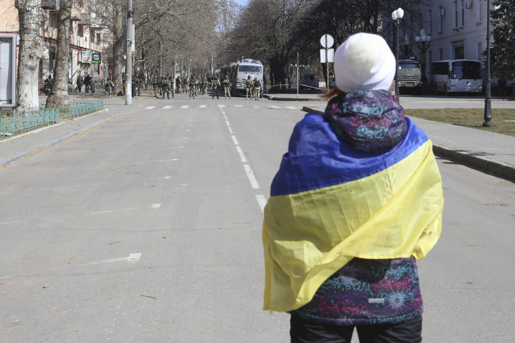 Žena s ukrajinskou vlajkou stojí pred ruskými vojakmi počas zhromaždenia proti ruskej okupácii v ukrajinskom meste Cherson.