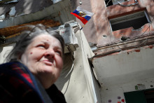 Žena kráča pozdĺž zničenej budovy v Mariupole, v ktorej ruinách je zapichnutá ruská vlajka. FOTO: Reuters