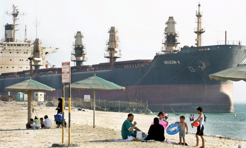 Rodina si užíva piknik na pláži kým ropný tanker čaká na prepravu ďalších miliónov ton čierneho zlata v Bahrajne. FOTO: Reuters