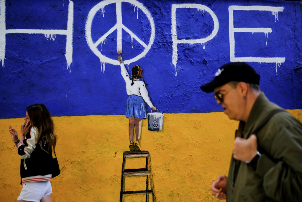 Ilustračn&aacute; n&aacute;stenn&aacute; maľba umelca TVBOY s farbami ukrajinskej vlajky a dievčaťa, ktor&eacute; maľuje symbol mieru. &Scaron;panielsko, 9. m&aacute;j 2022. FOTO: REUTERS/Nacho Doce