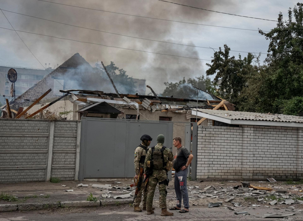 Policajti v Lysyčansku hovoria s miestnym obyvateľom počas toho, ako jeho dom po ruskom ostreľovaní horí. FOTO: REUTERS