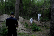 Policajt a členovia tímu v špeciálnom ochrannom odeve počas exhumácie tiel z masového hrobu v ukrajinskom meste Buča v Kyjevskej oblasti v pondelok 13. júna 2022. FOTO: TASR/AP


