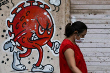 Žena prechádza okolo graffiti s tematikou koronavírusu uprostred šíriacej sa pandémie COVID-19 v Indii, 2021. FOTO: REUTERS