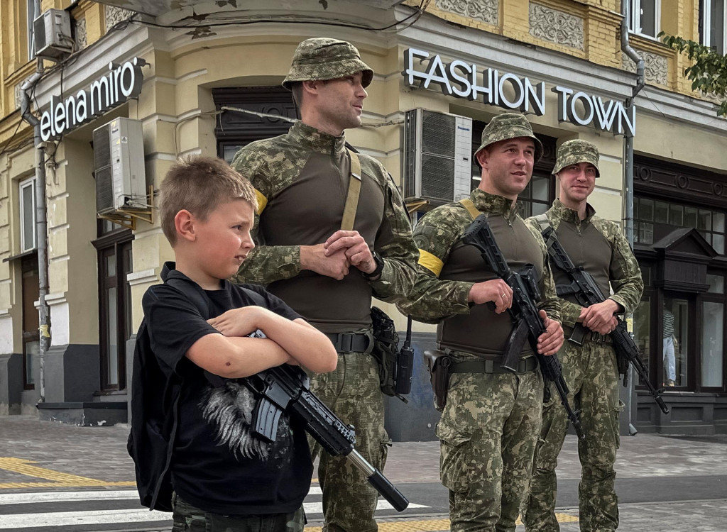 Chlapec s hračkárskym guľometom stojí v blízkosti ukrajinských vojakov, 22. júna 2022. FOTO: REUTERS/Gleb Garanich