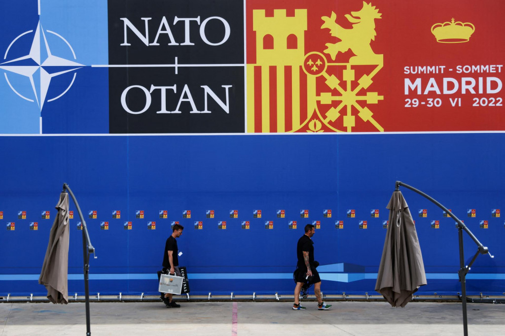 Technici z televízie prechádzajú okolo plagátu oznamujúceho summit NATO v Madride. FOTO: Reuters 