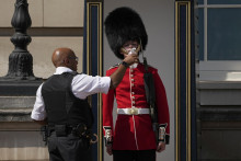 Policajt podáva vodu britskému vojakovi v tradičnom klobúku z medvedej kože, ktorý stojí spotený počas strážnej služby pred Buckinghamským palácom. FOTO: TASR/AP
