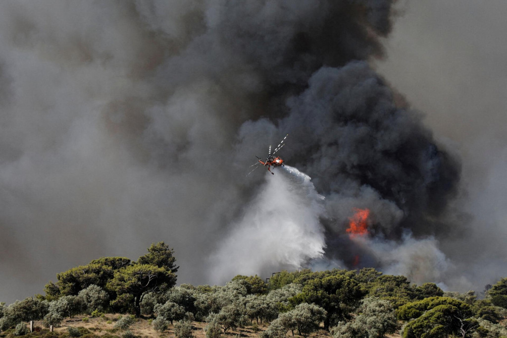 Hasičský vrtuľník zhadzuje vodu keďže horí lesný požiar na predmestí Pikermi v Aténach v Grécku, 20. júla 2022. FOTO: Reuters