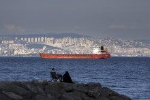 Na ilustračnej snímke z 13. júla 2022 rodina sedí na skale pred nákladnou loďou, ktorá kotví v Marmarskom mori a čaká na prístup cez úžinu Bospor v tureckom Istanbule. FOTO TASR/AP