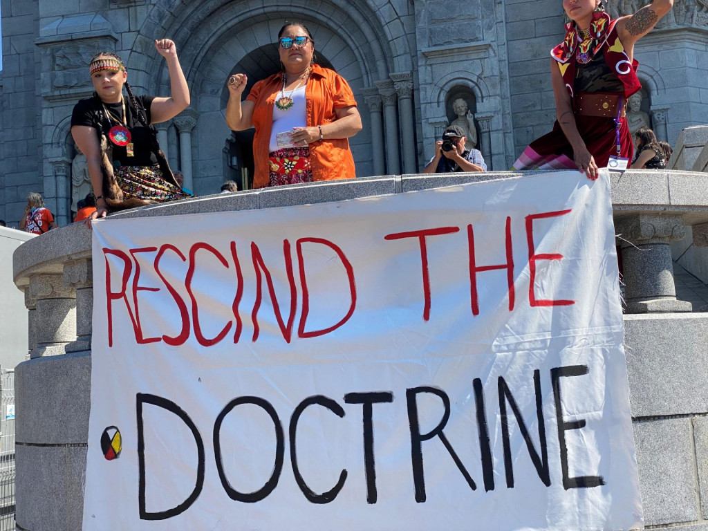 Ľudia držia transparent s nápisom „Zrušte doktrínu“ pred svätyňou Sainte-Anne-de-Beaupre. FOTO: Reuters/ Algonquin Chief Lance Haymond