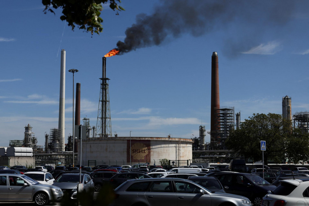 Autá parkujú pred olejovou nádržou Shell, zatiaľ čo plameň horí na hornom komíne v rafinérii spoločnosti. FOTO: Reuters