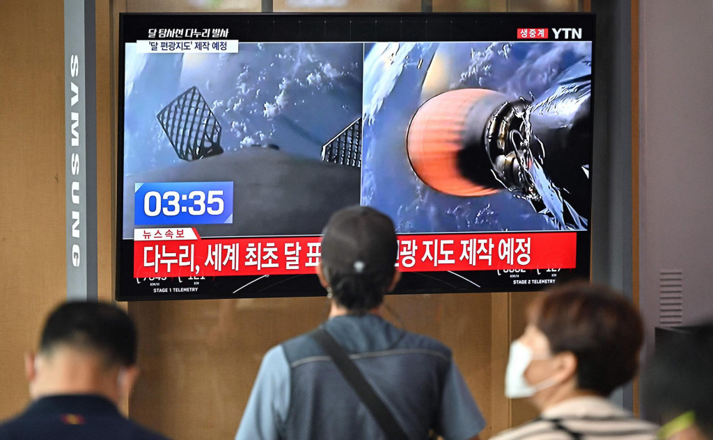 Ľudia sledujú televíznu obrazovku, ktorá ukazuje živé zábery štartu rakety SpaceX Falcon 9 s prvou juhokórejskou lunárnou orbiterkou Danuri. FOTO: Twitter/Bloomberg