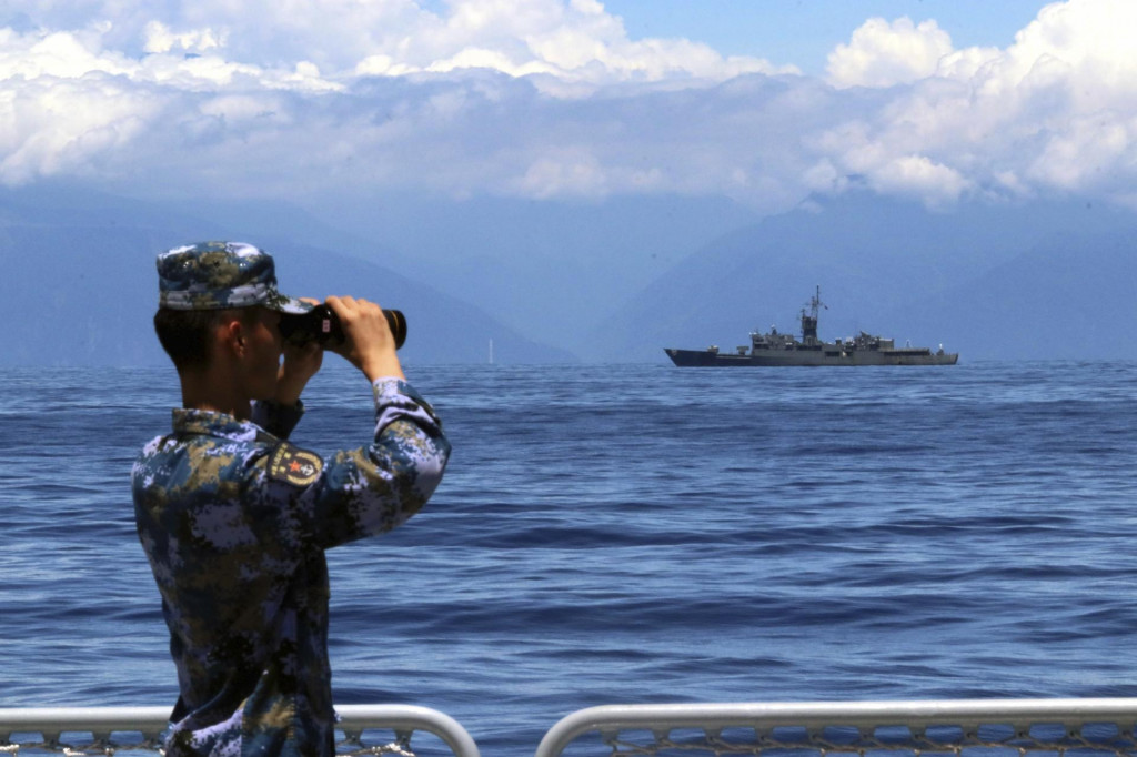 Vojak čínskej armády sa díva cez ďalekohľad, v pozadí pláva taiwanská vojenská loď. FOTO: TASR/AP
