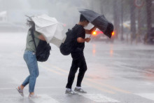 Chodci sa snažia chrániť dáždnikom počas silného vetra a dažďa v Soule. FOTO: TASR/Jonhap

