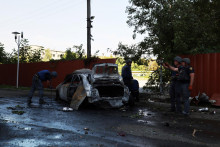 Policajti pracujú vedľa zničeného auta po ruskom vojenskom údere v Charkove. FOTO: Reuters