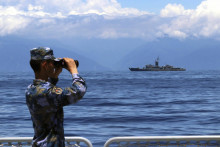Vojak čínskej armády sa díva cez ďalekohľad, kým v pozadí pláva taiwanská vojenská loď Lan Jang. FOTO: TASR/AP
