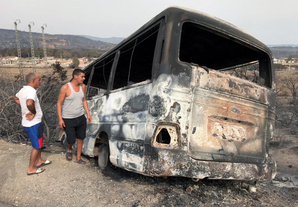 Muži kontrolujú autobus, ktorý zhorel po lesnom požiari v Alžírsku. FOTO: Reuters