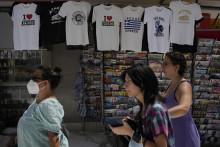 Ľudia kráčajú okolo obchodu s tričkami v Aténach. FOTO: TASR/AP