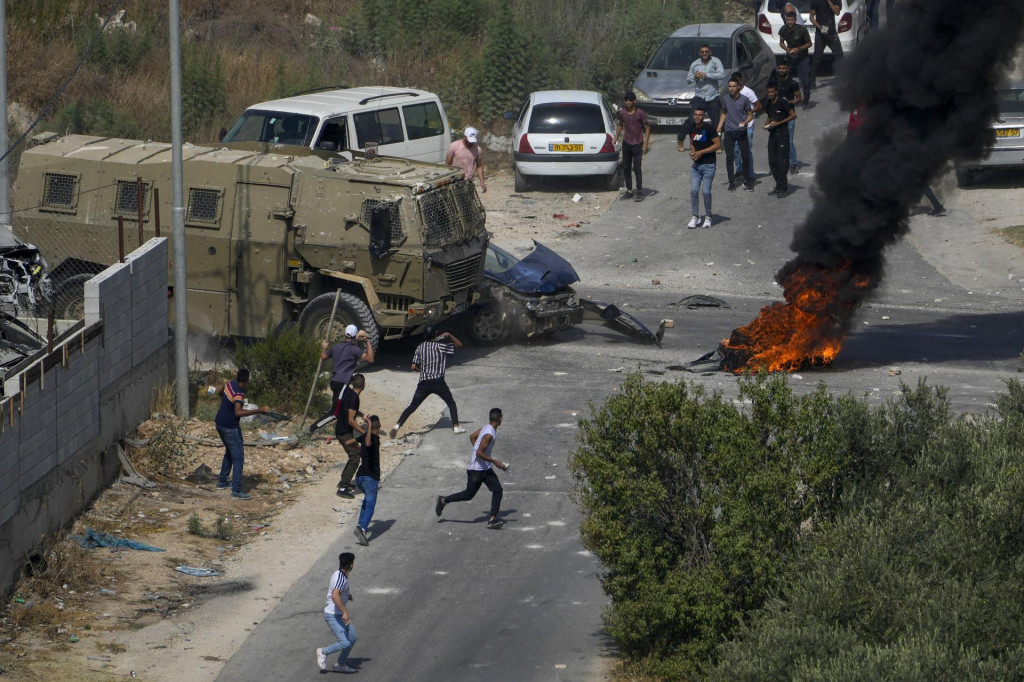 Palestínski demonštranti hádžu kamene na izraelské vojenské vozidlá. FOTO: TASR/AP