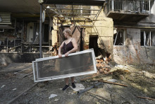 Žena nesie okenné rámy po ruskom útoku, ktorý poškodil niekoľko budov v ukrajinskom Charkove. FOTO: TASR/AP