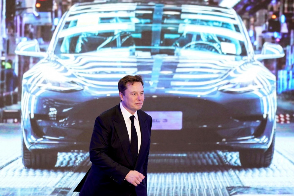 Generálny riaditeľ spoločnosti Tesla Elon Musk kráča vedľa obrazovky s obrázkom auta Tesla Model 3. FOTO: Reuters