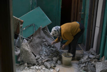 Staršia žena upratuje rozbité sklo z vchodu svojho bytu v obytnom dome, ktorý bol poškodený po ruskom útoku. FOTO: TASR/AP