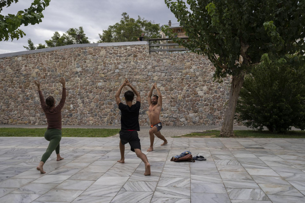 Ľudia cvičia jogu pri kamennom moste v historickej štvrti Thiseio v Aténach v Grécku. FOTO: TASR/AP