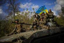 Ukrajinskí vojaci, ktorí sedia na obrnenom vozidle, držia ukrajinskú vlajku na ceste medzi nedávno oslobodenými mestami. FOTO: TASR/AP