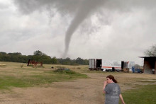 Žena kráča na farme a v pozadí je vidieť lievikovitý oblak tornáda v Greenview v Texase. FOTO: Reuters/Twitter @rcf_2008