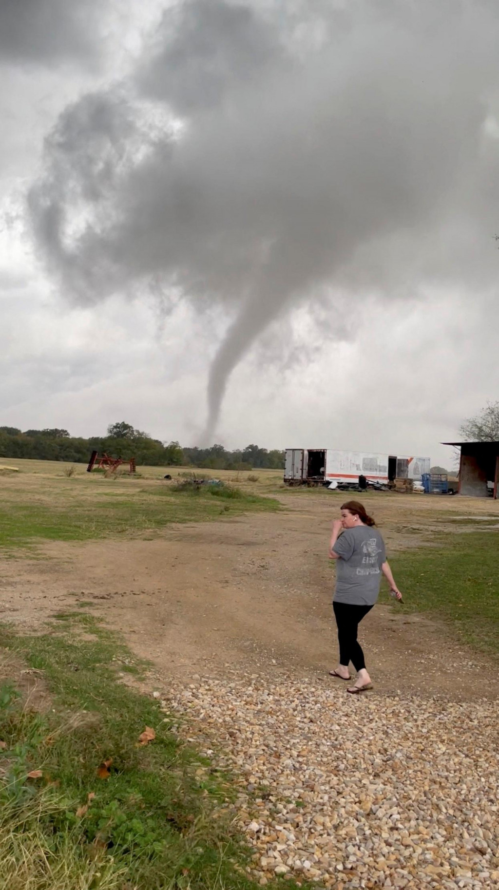 Žena kráča na farme a v pozadí je vidieť lievikovitý oblak tornáda v Greenview v Texase. FOTO: Reuters/Twitter @rcf_2008