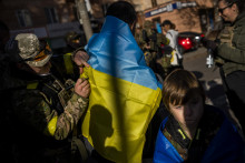 Na snímke príslušník ukrajinských obranných síl podpisuje ukrajinskú vlajku obyvateľovi v oslobodenom meste Cherson FOTO: TASR/AP