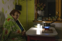 Staršia žena sedí zabalená v deke a varí jedlo na plynovom horáku počas výpadku elektriny v Kyjeve.  FOTO: TASR/AP
