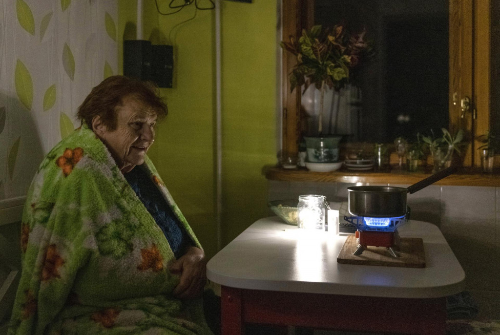 Staršia žena sedí zabalená v deke a varí jedlo na plynovom horáku počas výpadku elektriny v Kyjeve.  FOTO: TASR/AP