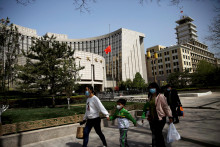 Ľudia v rúškach pred budovou všemocnej Ľudovej banky Číny v Pekingu. FOTO: Reuters