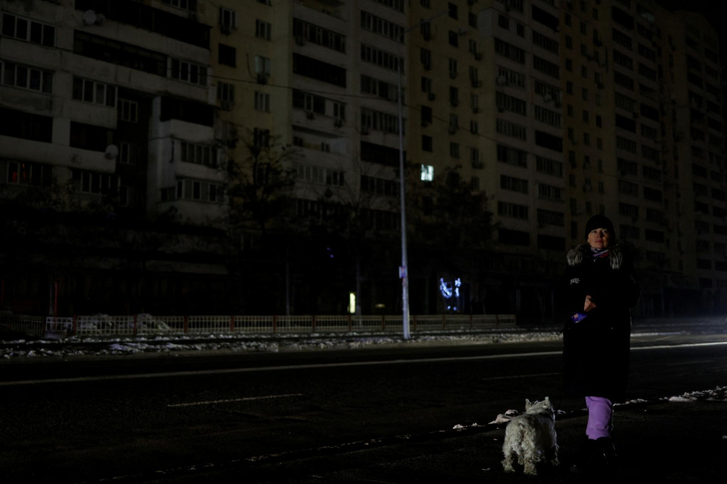 Žena so psom čaká na autobus na ulici bez elektriny po tom, čo kritickú civilnú infraštruktúru zasiahli ruské raketové útoky. FOTO: Reuters