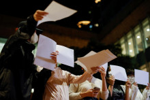 Ženy rozdávajú hárky papiera na protest proti obmedzeniam proti covidu v Číne počas spomienky na obete požiaru v Urumči. FOTO: REUTERS