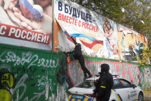 Ukrajinský policajt strháva ruské propagandistické bilbordy v Chersone. FOTO: REUTERS