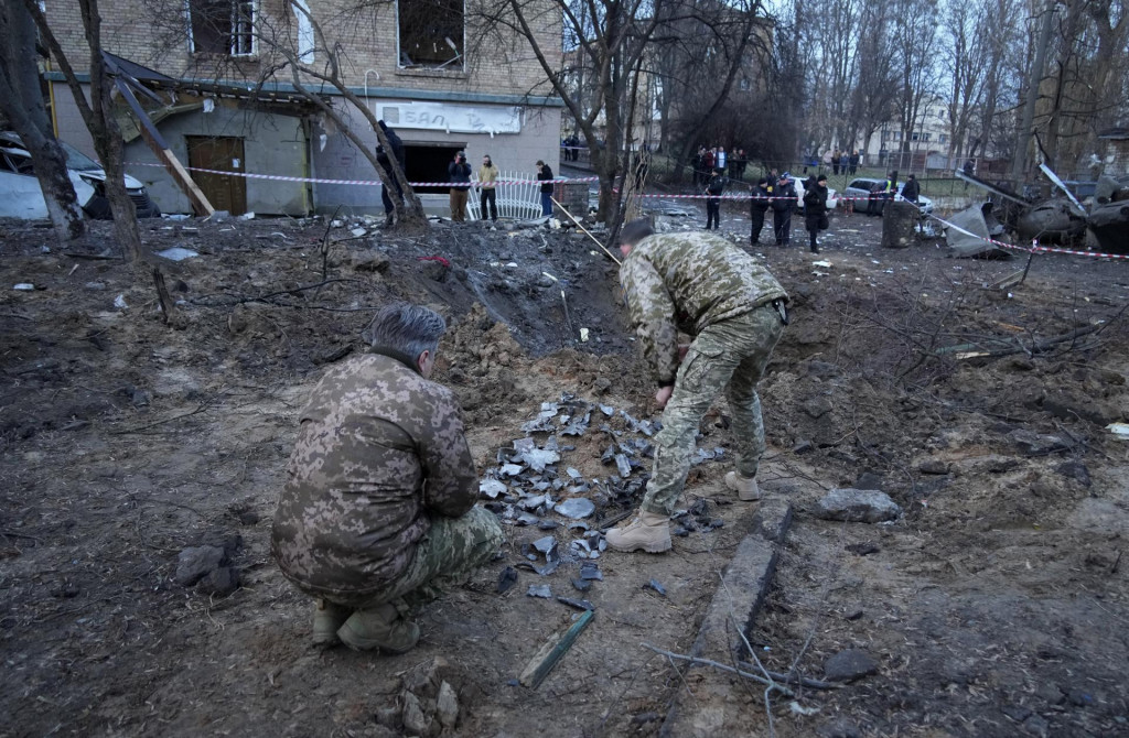 Policajní experti si prezerajú úlomky pred kráterom po ruskom raketovom útoku v Kyjeve v sobotu 31. decembra 2022.