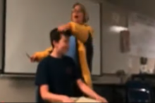Učiteľka strihá svojho študenta počas toho, ako spieva hymnu.