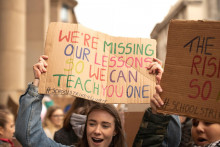 Mladé dievča drží banner s nápisom: ”Nie sme teraz na hodinách v škole, aby sme ťa mohli niečo naučiť.”