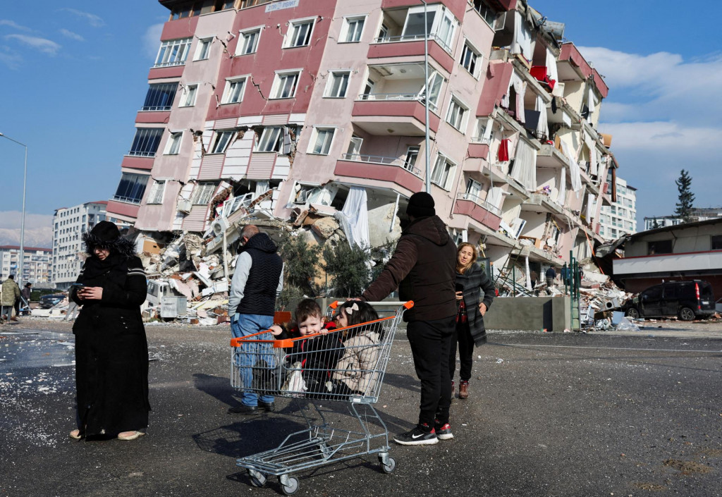Deti sedia v nákupnom košíku pri zrútenej budove po zemetrasení v Hatay v Turecku 7. februára 2023. REUTERS