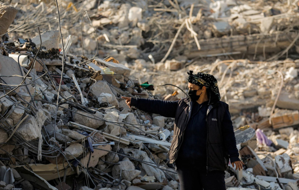 Turecká žena sprevádza fotografa popri hromade trosiek po smrteľnom zemetrasení v meste Hatay. FOTO: Reuters