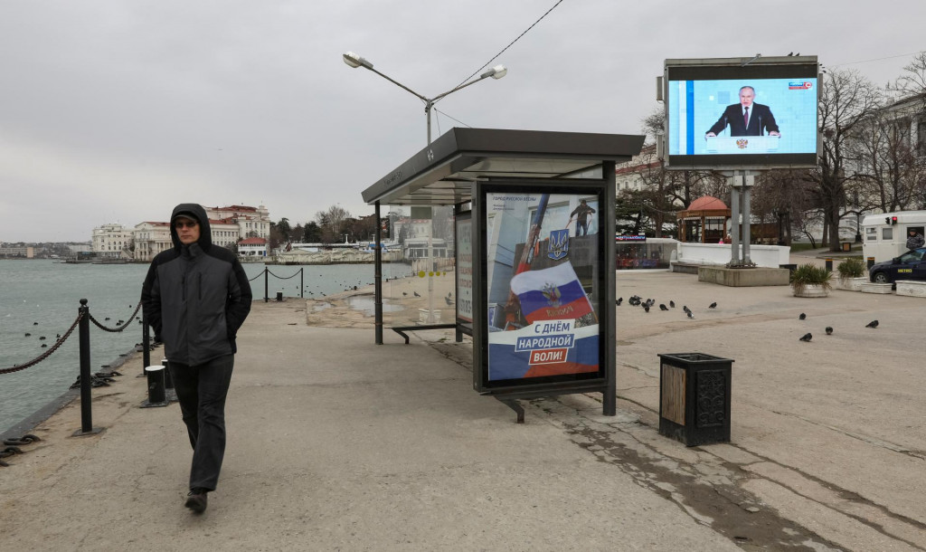 Muž kráča po nábreží v Sevastopole na Kryme, kým na obrazovke vidno Vladimira Putina počas jeho výročného prejavu vo Federálnom zhromaždení. FOTO: REUTERS