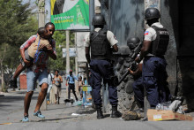 Muž nesie svojho syna a hľadá úkryt uprostred násilia gangov v Port-au-Prince v Haiti. FOTO: Reuters